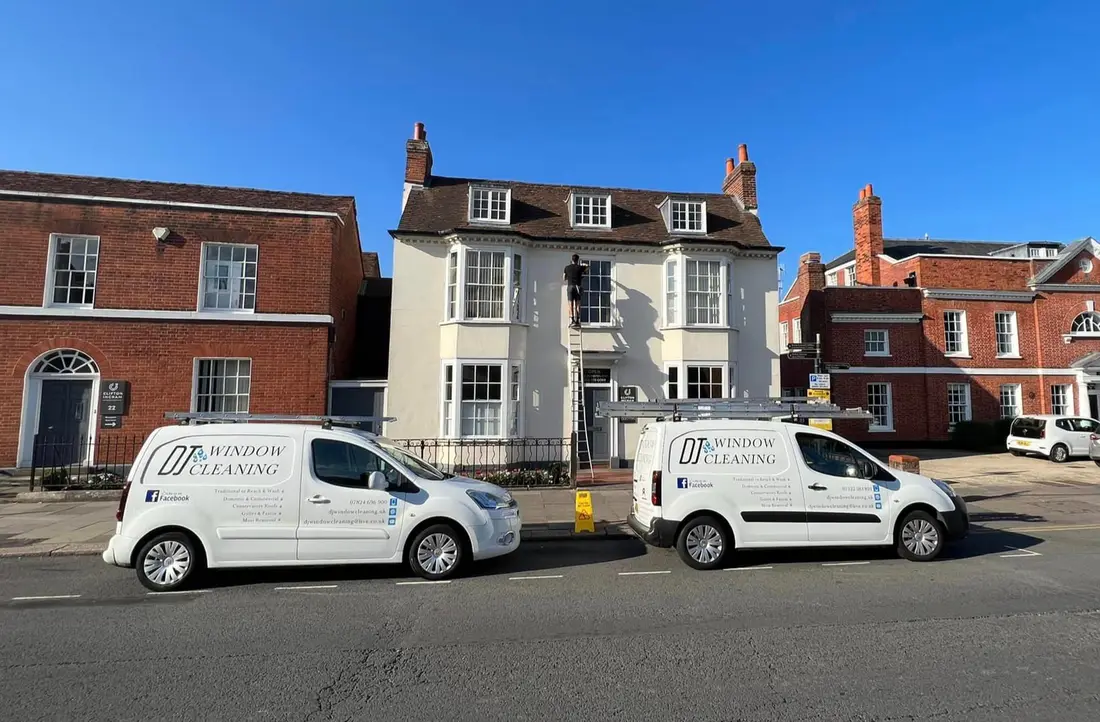 Two DJ Window Cleaning vans parked outside a period building