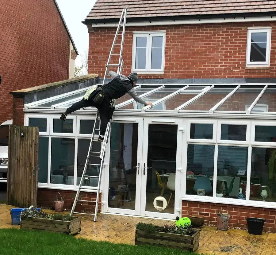 Cleaner working on a conservatory roof from a ladder