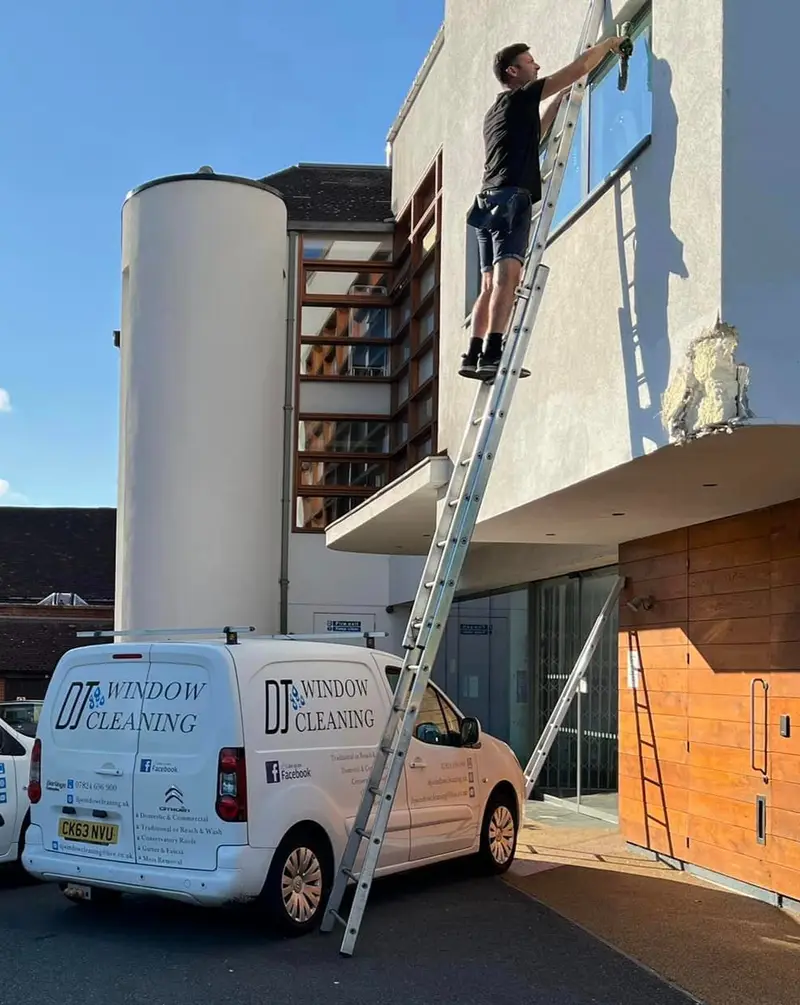 Cleaning high windows on a commercial building from a ladder